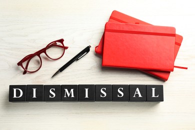 Image of Word Dismissal made of black cubes, pen, eyeglasses and notebooks on white wooden background, top view