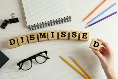 Image of Woman making word Dismissed with wooden cubes at white table, top view