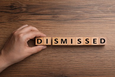 Image of Woman making word Dismissed with cubes on wooden table, top view