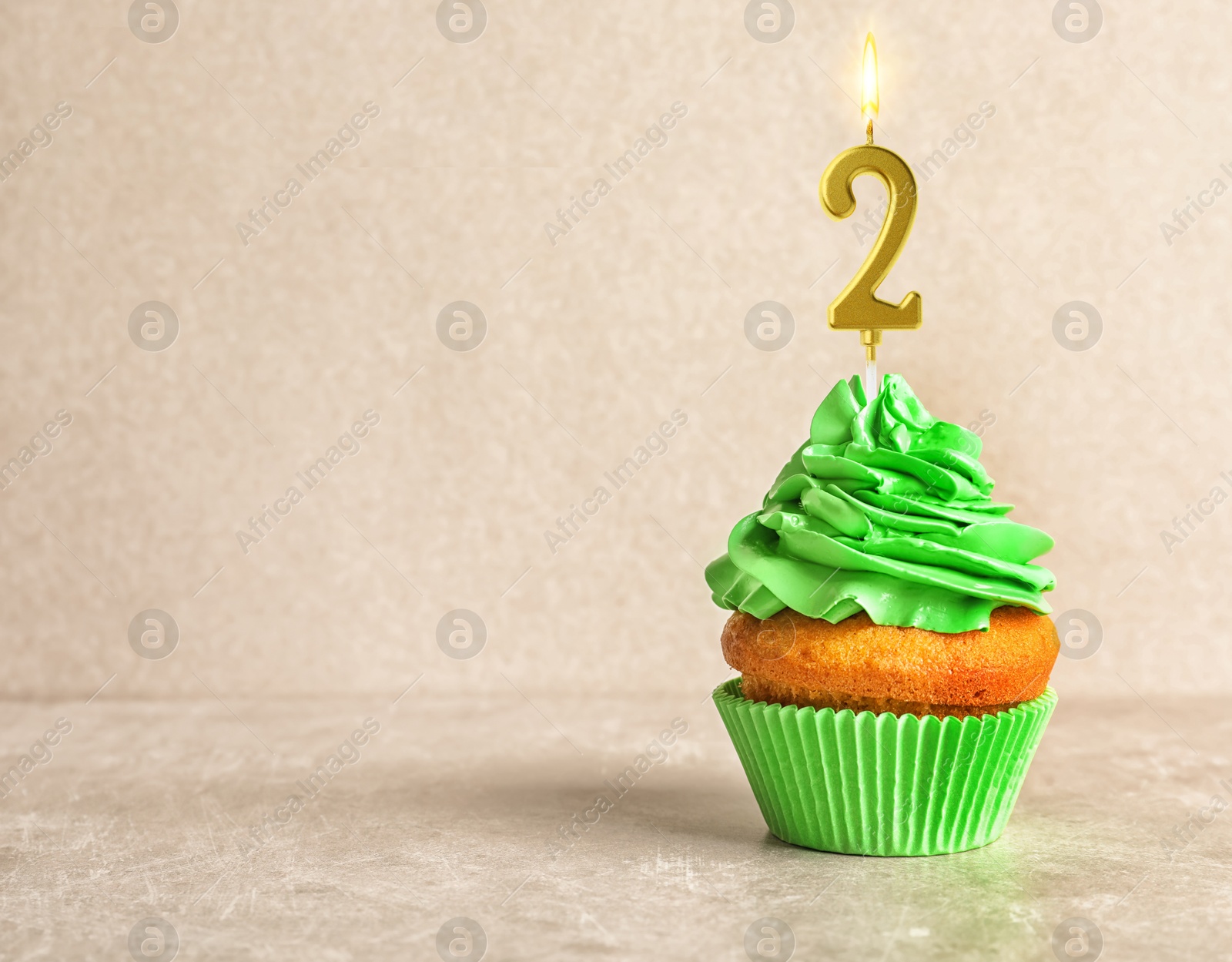 Yummy cupcake with burning golden candle in shape of number 2 on beige background, space for text. Birthday or other special occasion Image of Yummy cupcake with burning golden candle in shape of number 2 on beige background, space for text. Birthday or other special occasion