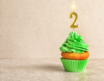 Image of Yummy cupcake with burning golden candle in shape of number 2 on beige background, space for text. Birthday or other special occasion