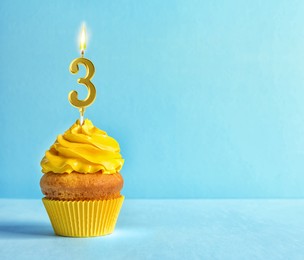 Image of Yummy cupcake with burning golden candle in shape of number 3 on light blue background, space for text. Birthday or other special occasion