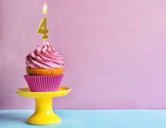 Image of Yummy cupcake with burning golden candle in shape of number 4 on table against violet background, space for text. Birthday or other special occasion