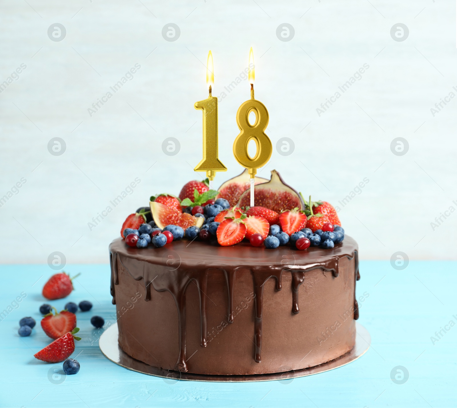 Yummy chocolate cake with fruits and burning number shaped candles on light blue table. 18th birthday or other special occasion Image of Yummy chocolate cake with fruits and burning number shaped candles on light blue table. 18th birthday or other special occasion