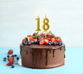 Image of Yummy chocolate cake with fruits and burning number shaped candles on light blue table. 18th birthday or other special occasion