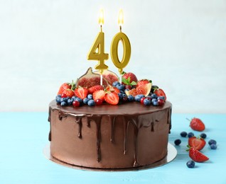 Image of Yummy chocolate cake with fruits and burning number shaped candles on light blue table. 40th birthday or other special occasion