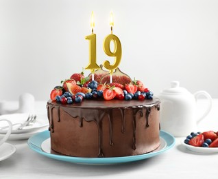 Image of Yummy chocolate cake with fruits and burning number shaped candles on white table. 19th birthday or other special occasion