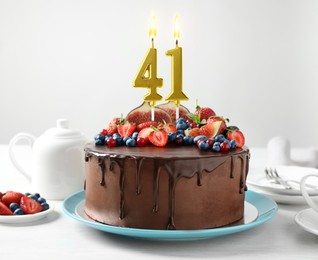 Image of Yummy chocolate cake with fruits and burning number shaped candles on white table. 41th birthday or other special occasion