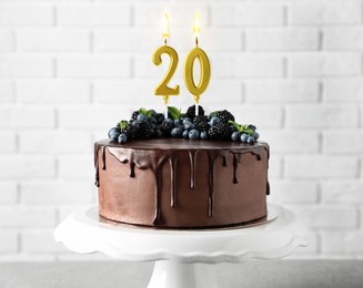 Image of Yummy chocolate cake with berries and burning number shaped candles on table. 20th birthday or other special occasion