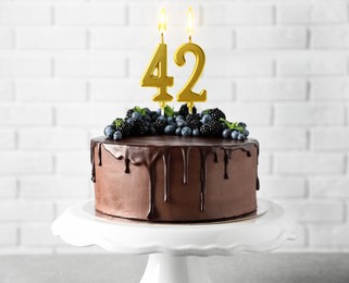 Image of Yummy chocolate cake with berries and burning number shaped candles on table. 42th birthday or other special occasion