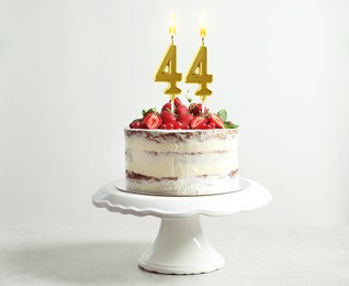 Image of Yummy cake with fruits and burning number shaped candles on white background. 44th birthday or other special occasion