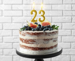 Image of Yummy cake with fruits and burning number shaped candles near white brick wall. 23th birthday or other special occasion