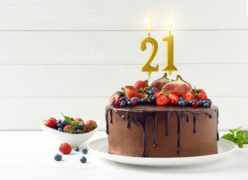 Image of Yummy chocolate cake with fruits and burning number shaped candles on white table, space for text. 21th birthday or other special occasion