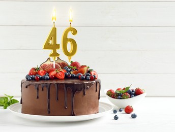 Image of Yummy chocolate cake with fruits and burning number shaped candles on white table, space for text. 46th birthday or other special occasion