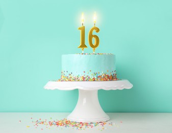Image of Yummy cake with burning number shaped candles and sprinkles on white table against turquoise background. 16th birthday or other special occasion