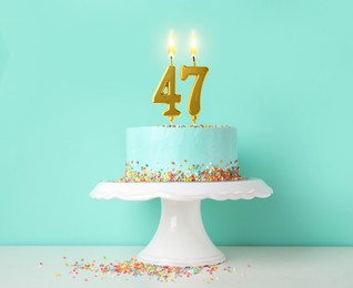 Image of Yummy cake with burning number shaped candles and sprinkles on white table against turquoise background. 47th birthday or other special occasion