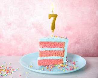 Image of Piece of yummy cake with burning golden candle in shape of number 7 and sprinkles on table. Birthday or other special occasion