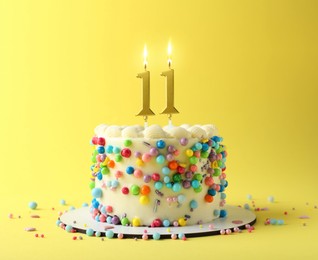 Image of Yummy cake with burning number shaped candles and sprinkles on yellow background. 11th birthday or other special occasion