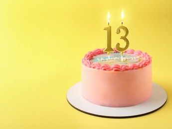 Image of Yummy cake with burning number shaped candles on yellow background, space for text. 13th birthday or other special occasion