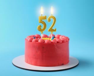 Image of Yummy cake with burning number shaped candles on light blue background. 52th birthday or other special occasion
