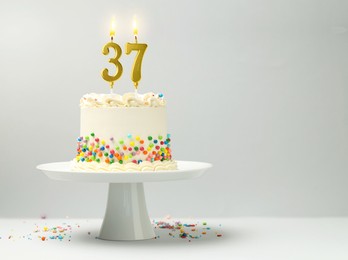 Image of Yummy cake with burning number shaped candles and sprinkles on light background, space for text. 37th birthday or other special occasion