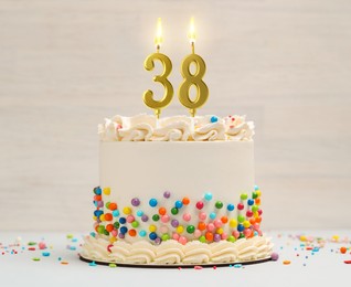 Image of Yummy cake with burning number shaped candles and sprinkles on light background. 38th birthday or other special occasion