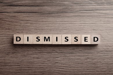Image of Word Dismissed made of cubes on wooden background, top view