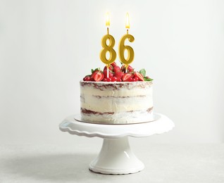 Image of Yummy cake with fruits and burning number shaped candles on white background. 86th birthday or other special occasion