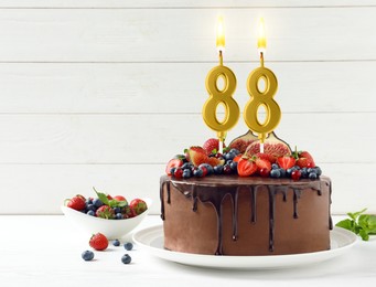 Image of Yummy chocolate cake with fruits and burning number shaped candles on table, space for text. 88th birthday or other special occasion