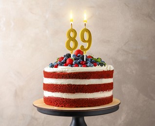 Image of Yummy cake with berries and burning number shaped candles near grey wall. 89th birthday or other special occasion