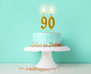 Image of Yummy cake with burning number shaped candles and sprinkles on white table against turquoise background. 90th birthday or other special occasion