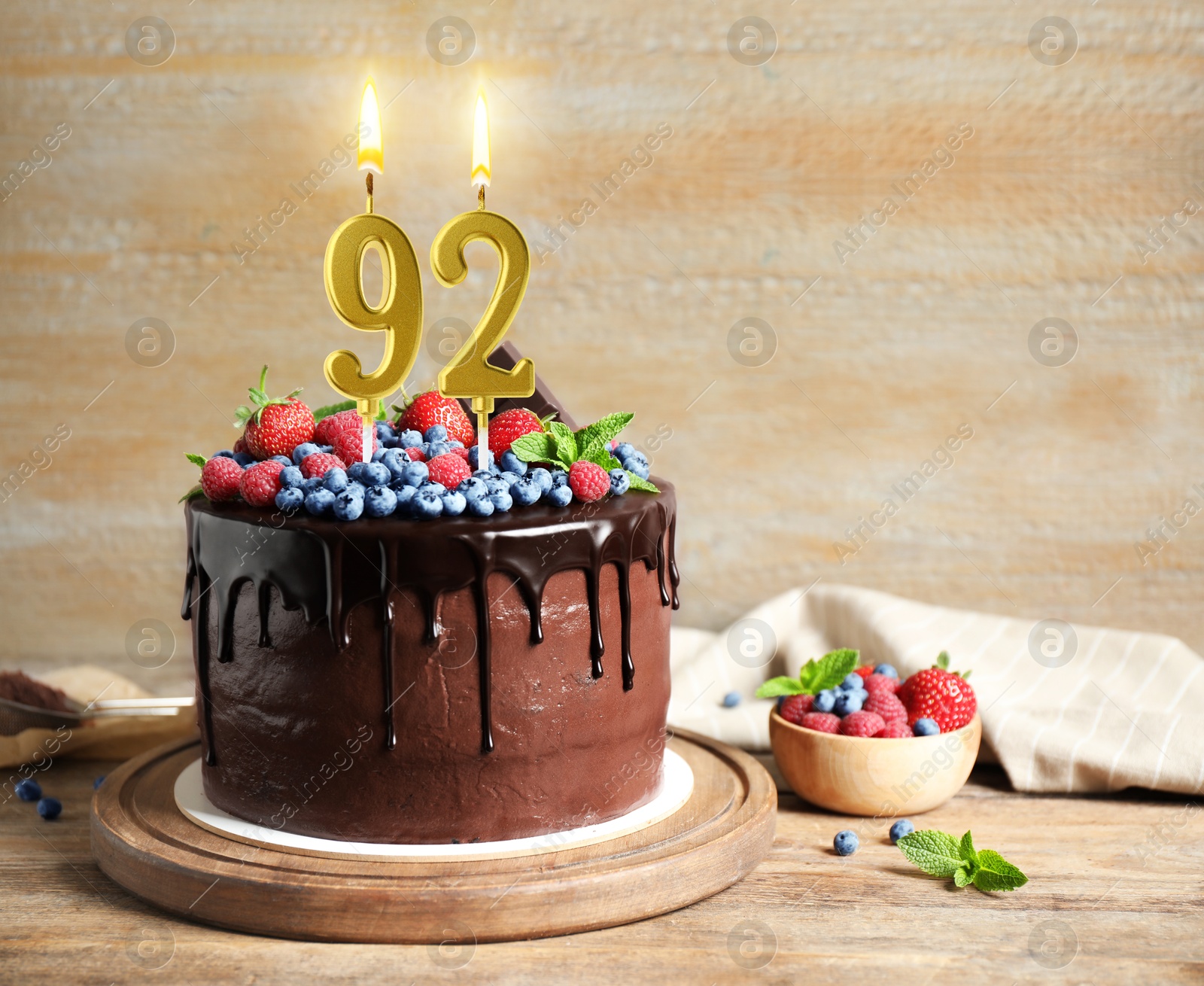 Yummy chocolate cake with berries and burning number shaped candles on wooden table, space for text. 92th birthday or other special occasion Image of Yummy chocolate cake with berries and burning number shaped candles on wooden table, space for text. 92th birthday or other special occasion