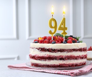 Image of Yummy cake with berries and burning number shaped candles on light table. 94th birthday or other special occasion