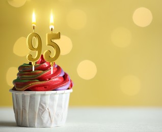 Image of Yummy cupcake with burning number shaped candles on yellow background with blurred lights, space for text. 95th birthday or other special occasion