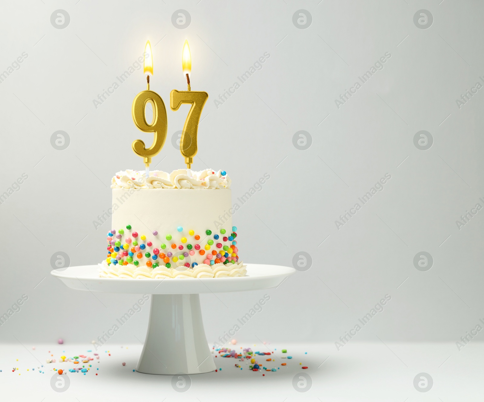 Yummy cake with burning number shaped candles and sprinkles on light background, space for text. 97th birthday or other special occasion Image of Yummy cake with burning number shaped candles and sprinkles on light background, space for text. 97th birthday or other special occasion