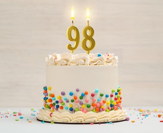 Image of Yummy cake with burning number shaped candles and sprinkles on light background. 98th birthday or other special occasion