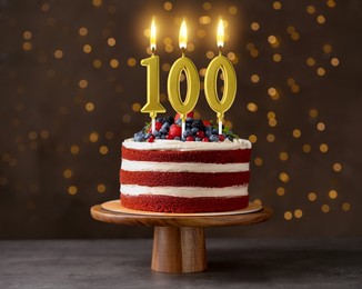 Image of Yummy cake with berries and burning number shaped candles on table against dark background with blurred lights. 100th birthday or other special occasion
