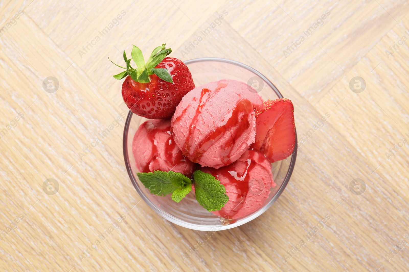 Photo of Refreshing sorbet with syrup, strawberries and mint in bowl on wooden table, top view