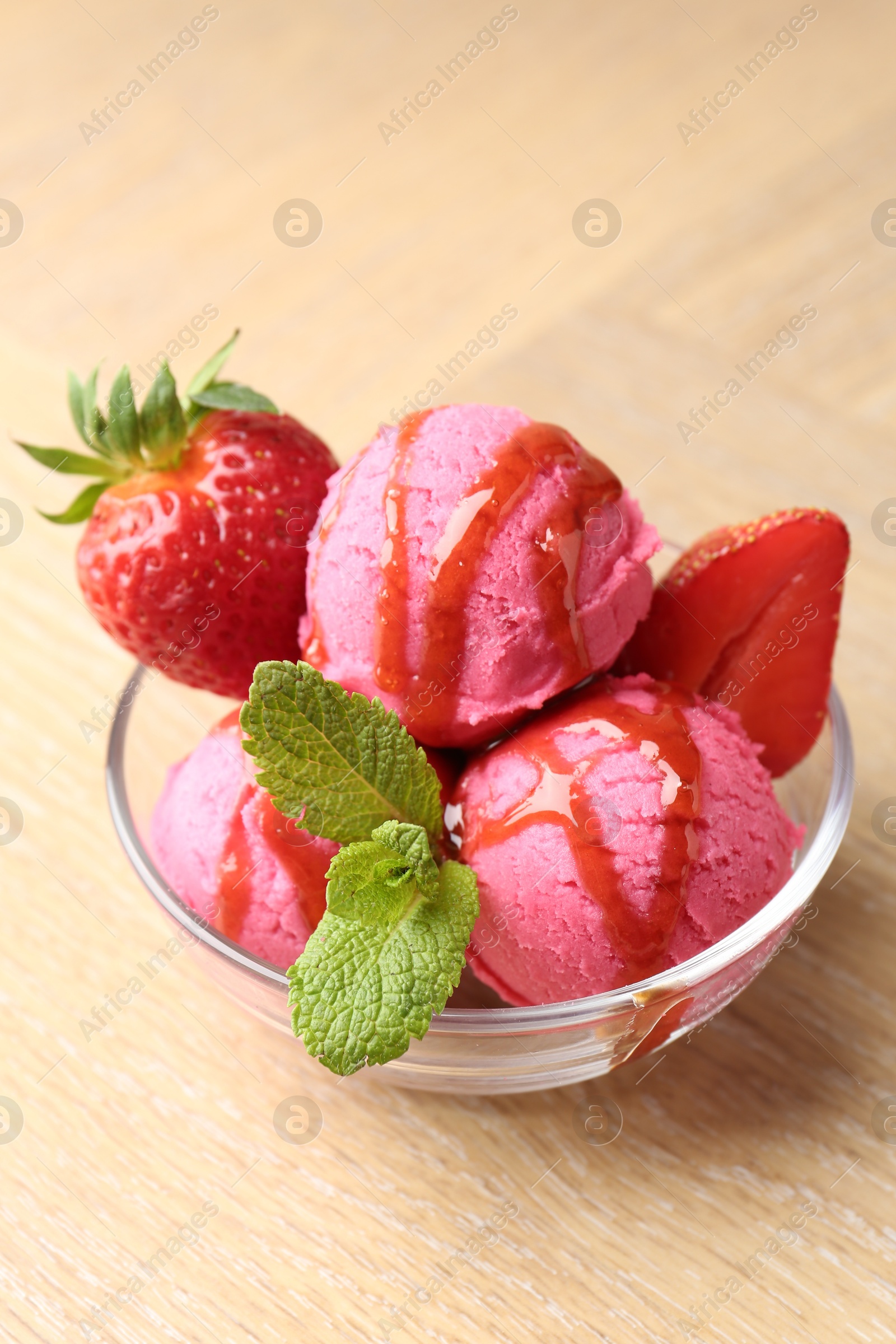 Photo of Refreshing sorbet with syrup, strawberries and mint in bowl on wooden table