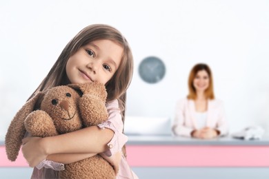Image of Cute little girl with toy bunny in lobby of children's hospital. Receptionist at desk