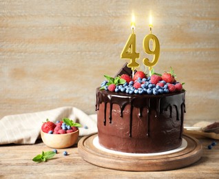 Image of Yummy chocolate cake with berries and burning number shaped candles on wooden table, space for text. 49th birthday or other special occasion