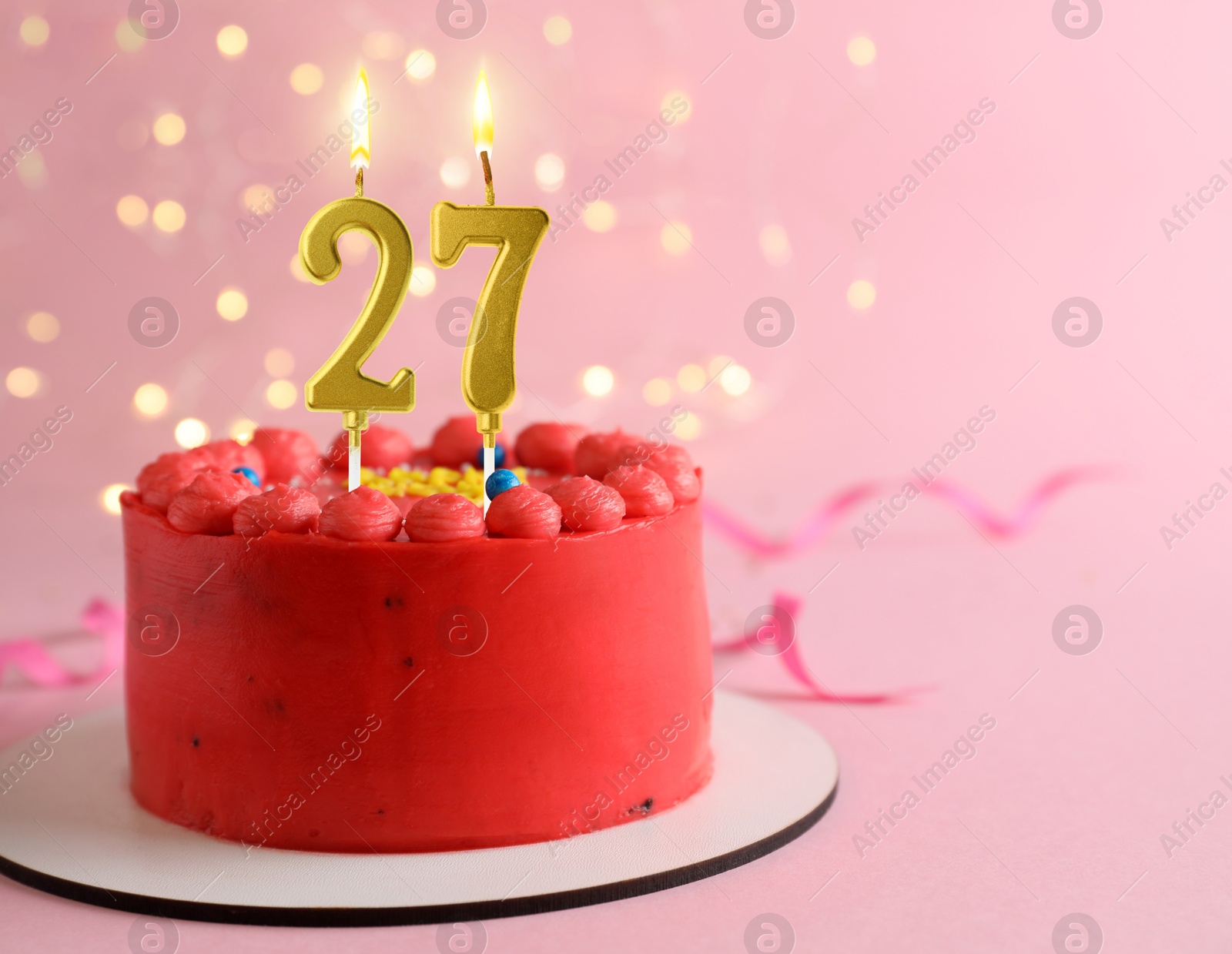 Image of Yummy cake with burning number shaped candles on pink background with blurred lights, space for text. 27th birthday or other special occasion