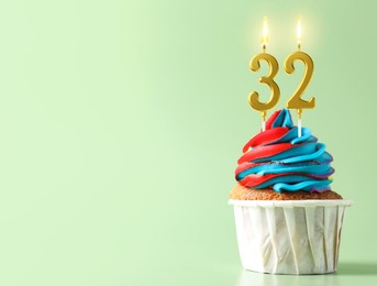 Image of Yummy cupcake with burning number shaped candles on light turquoise background, space for text. 32th birthday or other special occasion