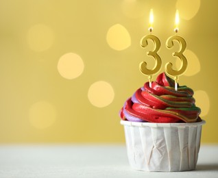 Image of Yummy cupcake with burning number shaped candles on yellow background with blurred lights, space for text. 33th birthday or other special occasion