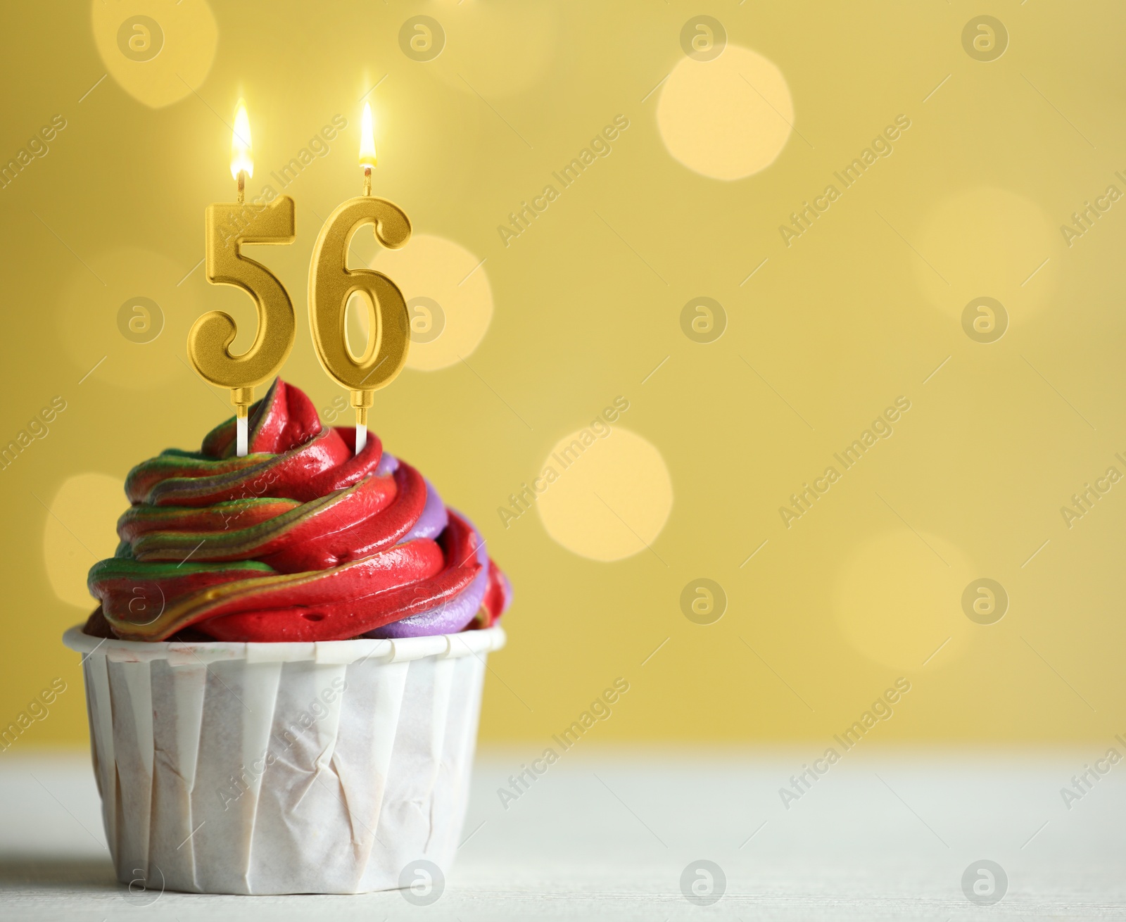 Image of Yummy cupcake with burning number shaped candles on yellow background with blurred lights, space for text. 56th birthday or other special occasion
