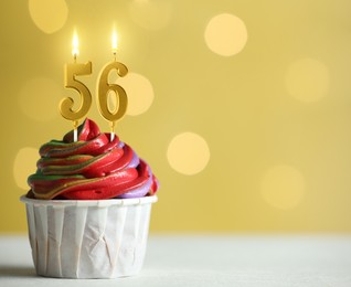 Image of Yummy cupcake with burning number shaped candles on yellow background with blurred lights, space for text. 56th birthday or other special occasion