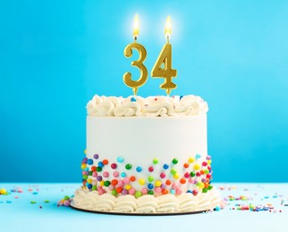 Image of Yummy cake with burning number shaped candles and sprinkles on light blue background. 34th birthday or other special occasion