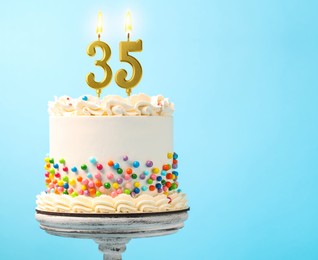 Image of Yummy cake with sprinkles and burning number shaped candles on light blue background, space for text. 35th birthday or other special occasion
