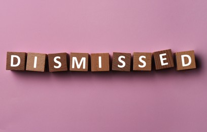 Image of Word Dismissed made of wooden cubes on pink background, top view