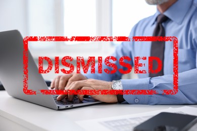 Image of Man using laptop at table and red stamp Dismissed, closeup